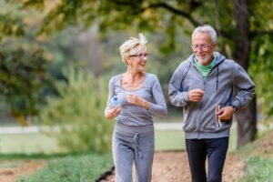 Cuplu de adulți în vârstă care aleargă într-un parc, ilustrând longevitatea sănătoasă